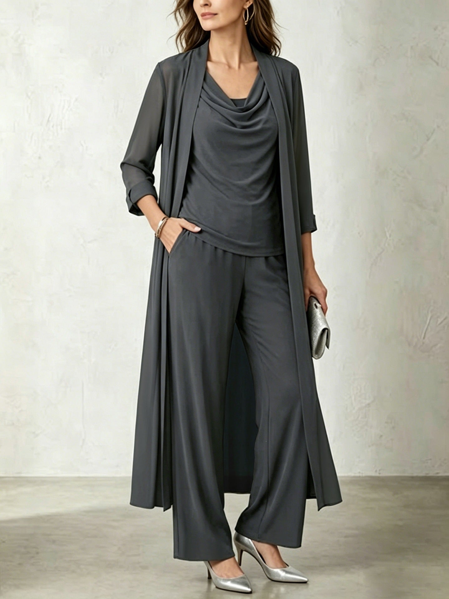 Model wearing a carbon gray three-piece cardigan and wide-leg pant set, accessorized with metallic silver pointy-toe pumps and a matching clutch.