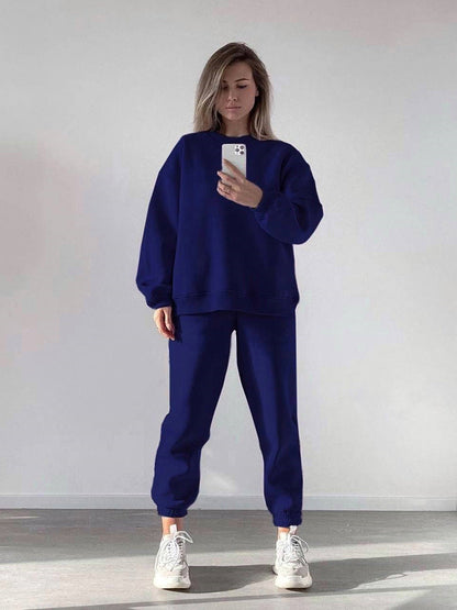 Woman wearing a blue loose-fit crewneck sweatshirt and matching jogger pants two-piece set, styled with white sneakers.