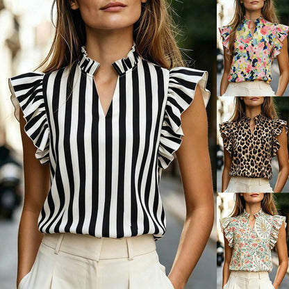 Woman wearing a black-and-white striped sleeveless top with a high ruffle-trim mock neck and lotus-leaf ruffle sleeves, styled with white high-waist pants.