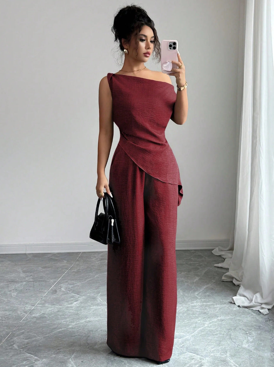 Woman taking a mirror selfie wearing a wine red casual two piece set featuring a draped off-the-shoulder top with a diagonal front fold and matching high-waisted wide-leg pants, holding a black handbag and white smartphone.