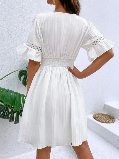 Back view of a woman wearing a white V-neck mini dress featuring short flounce sleeves with crochet lace trim, vertical textured striping, and a cinched lace waistband.