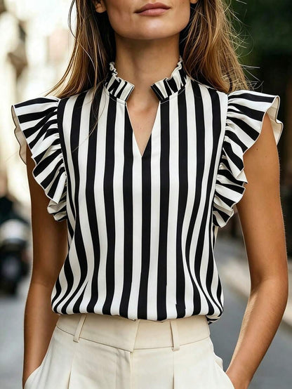 Woman wearing a black-and-white striped sleeveless top with a high ruffle-trim mock neck and lotus-leaf ruffle sleeves, styled with cream high-waist pants.