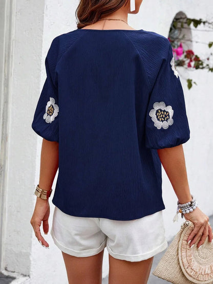 Back view of a woman wearing a navy blue top with floral embroidered sleeves and white cuffed shorts