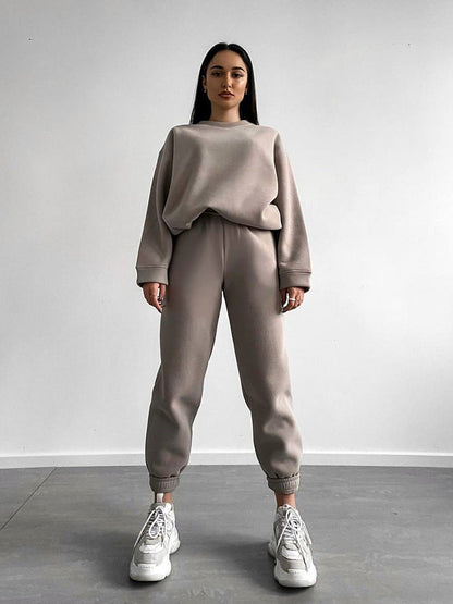 Woman wearing a camel loose-fit crewneck sweatshirt and matching jogger pants two-piece set, styled with white sneakers.