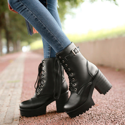 Woman wearing black chunky-heel lace-up Martin boots and blue jeans, walking on an outdoor pathway.
