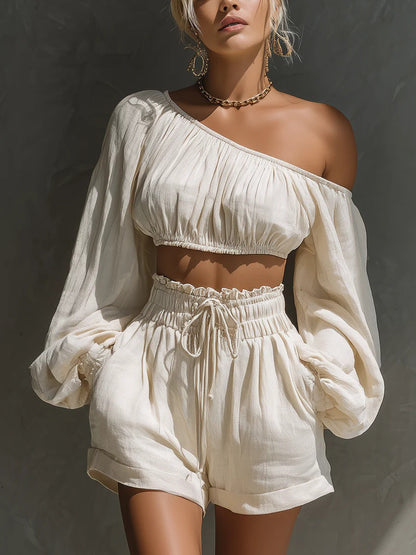 Close-up view of the white one-shoulder ruched crop top, highlighting the gathered neckline, billowy long sleeves, and gold chain necklace accessory.
