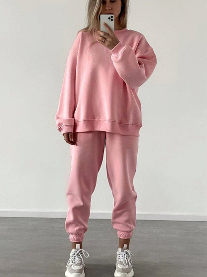 Woman wearing a pink loose-fit crewneck sweatshirt and matching jogger pants two-piece set, taking a mirror selfie with a smartphone.