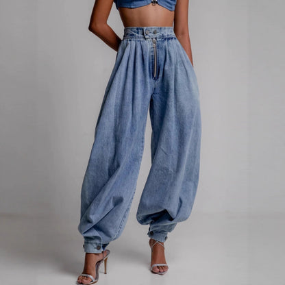 High-waisted light blue denim harem pants featuring a exposed front zipper, pleated waist, and cinched ankle ties, paired with strappy heeled sandals.