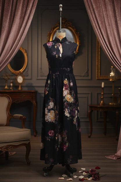 Black floral maxi dress displayed on a mannequin in an elegant vintage-style room with draped curtains, ornate mirrors, and scattered rose petals.