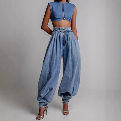 Woman wearing a light blue denim two-piece set featuring a sleeveless cropped top with a front zipper and high-waisted pleated harem pants with cinched ankle ties, paired with silver metallic heeled sandals.