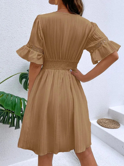 Back view of a woman wearing a camel brown V-neck mini dress with short flounce sleeves featuring crochet lace trim, textured vertical striping, and a cinched lace waistband.