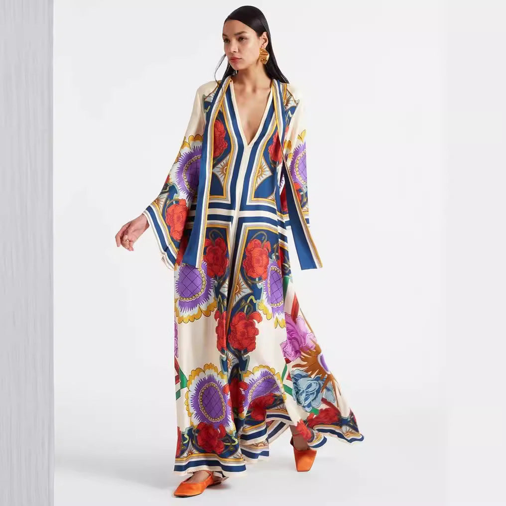 Full-length model shot of an off-white printed maxi dress featuring a vibrant botanical and floral pattern with blue border accents, a plunging V-neckline, and wide 3/4 flared sleeves.