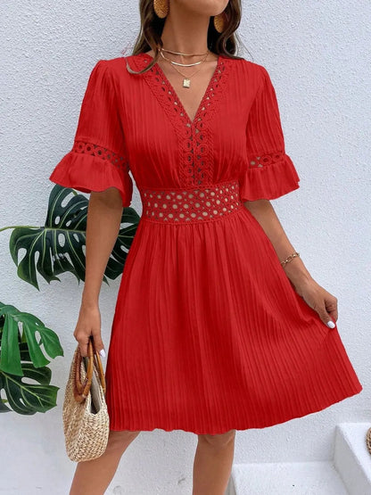 Flat lay view of a red V-neck mini dress with textured vertical striping, featuring crochet lace trim along the neckline, waist cutouts, and flounce sleeve cuffs, styled with layered gold necklaces, hoop earrings, and a woven straw handbag.