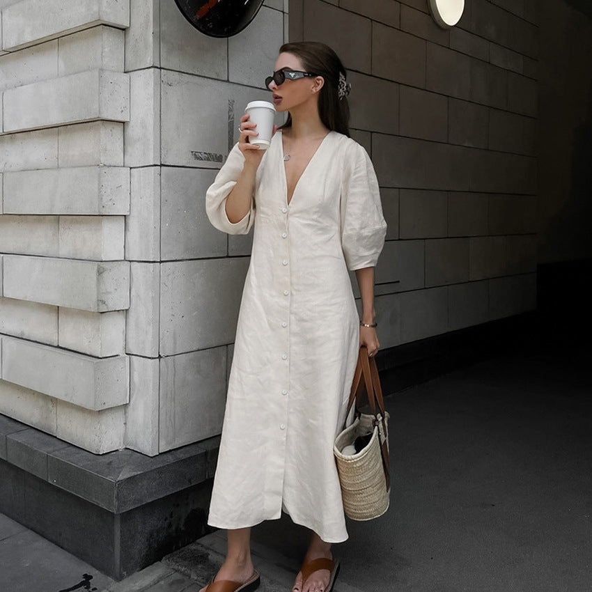 Full-length view of a woman outdoors wearing a light blue off-the-shoulder floral midi dress with white high heels and holding a beige handbag.