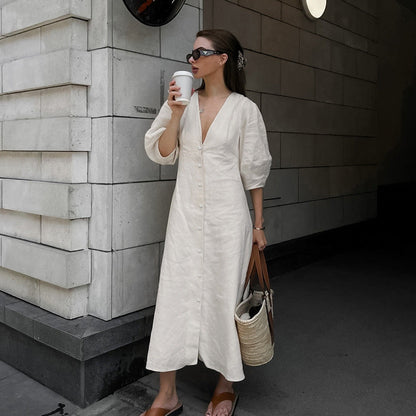 Full-length view of a woman outdoors wearing a light blue off-the-shoulder floral midi dress with white high heels and holding a beige handbag.