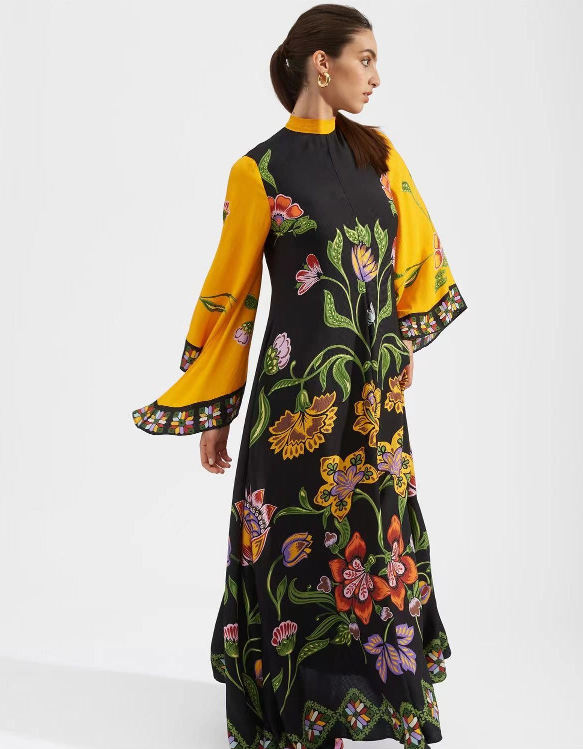 Women's floor-length A-line maxi dress in vibrant mustard yellow featuring a magenta and turquoise floral motif print, high mock stand collar, wide 3/4 flared sleeves, and decorative magenta border trim.