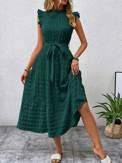 Front view of model stepping forward wearing a dark green ruffled cap sleeve midi dress with a tied waist and white slide sandals