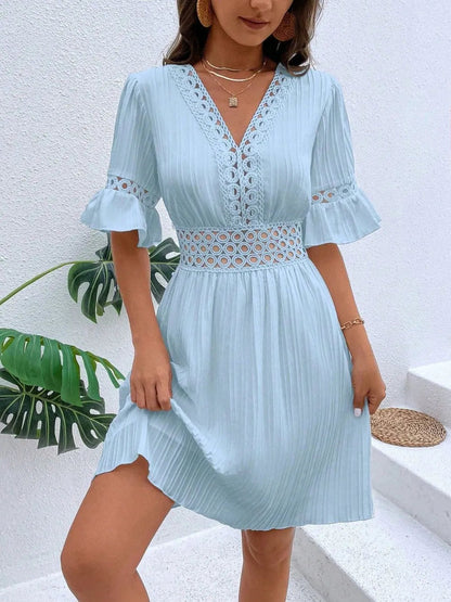 Woman wearing a light blue V-neck mini dress with vertical texture, featuring crochet lace waistband details and lace-trimmed flounce sleeves, styled with layered gold necklaces.