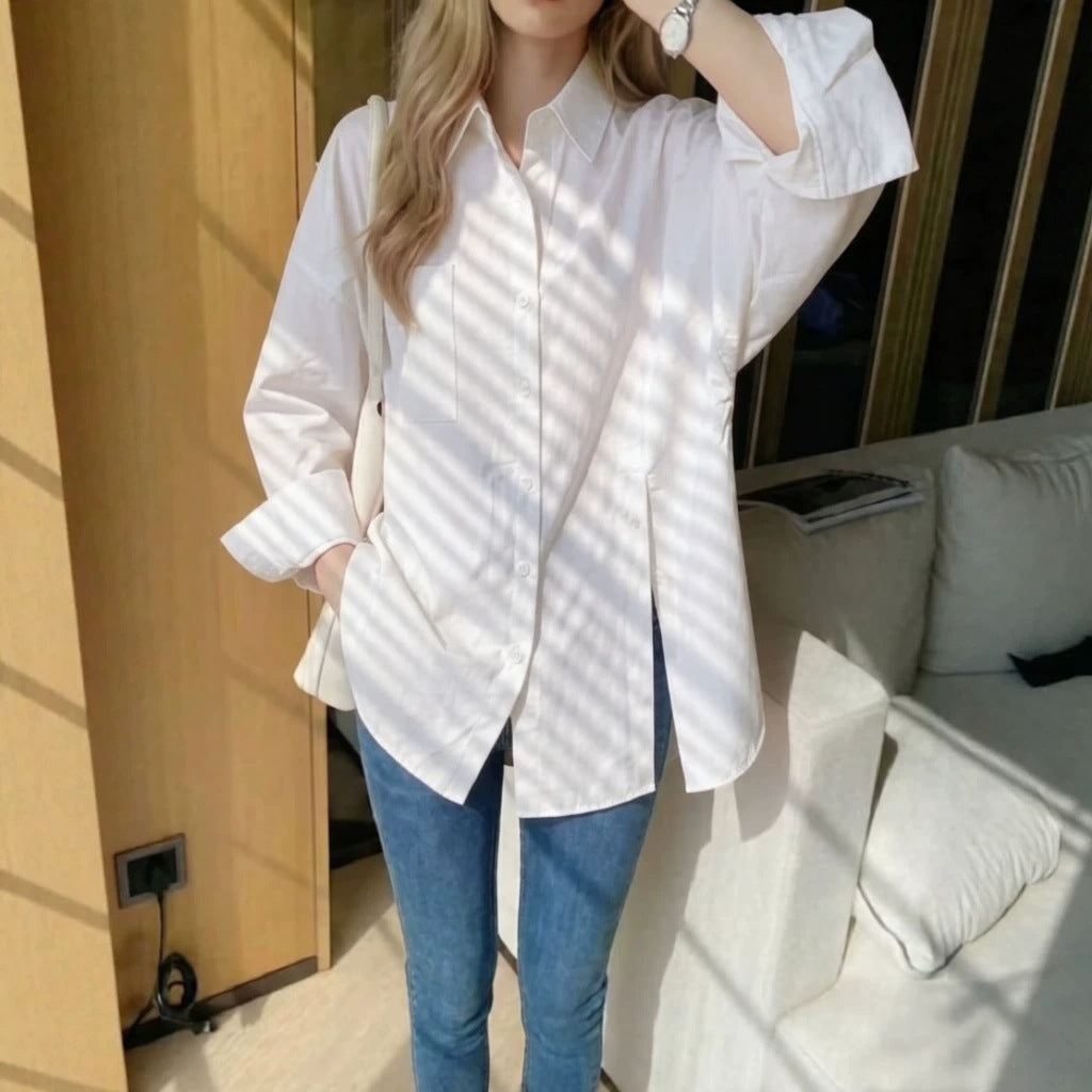 Woman wearing a white oversized long sleeve button-up shirt with drop shoulders and a side slit, paired with blue jeans.