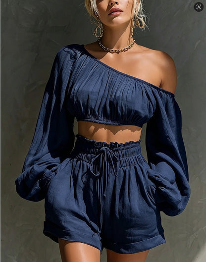 Model wearing the Women's One-Shoulder Ruched Crop Top & High-Waist Shorts Set in navy blue, featuring a gathered one-shoulder neckline, billowy long sleeve, and high-waist drawstring shorts.