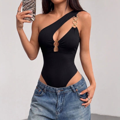 Front-facing close-up of a model wearing a black asymmetric off-shoulder hollow-out jumpsuit with gold ring strap hardware and denim.