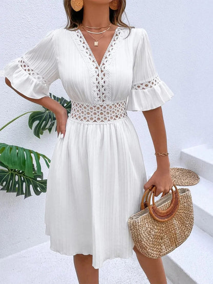 Woman wearing a white V-neck mini dress with textured vertical stripe details, featuring crochet lace waist cutouts, short lace-trimmed flounce sleeves, and layered pendant necklaces.