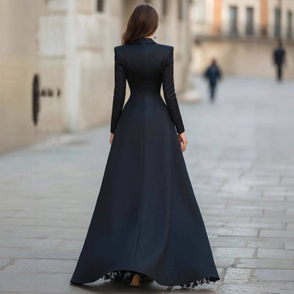 Rear view of a women's elegant black formal outfit featuring a structured long-sleeve jacket top with padded shoulders and a floor-length A-line skirt.
