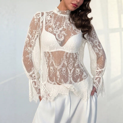 Woman wearing a sheer white lace hollow-out long sleeve top with a mock neck and white trousers.