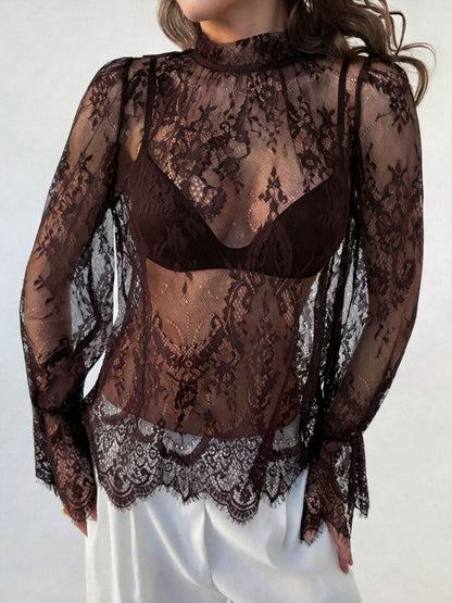 Close-up front view of a woman wearing a sheer black lace hollow-out long sleeve top featuring a mock neck and intricate floral pattern.