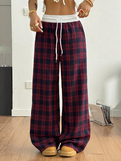 Front view of high-waisted red and dark blue plaid straight-leg sweatpants featuring a white elastic contrast waistband with a white drawstring, styled with tan sneakers.