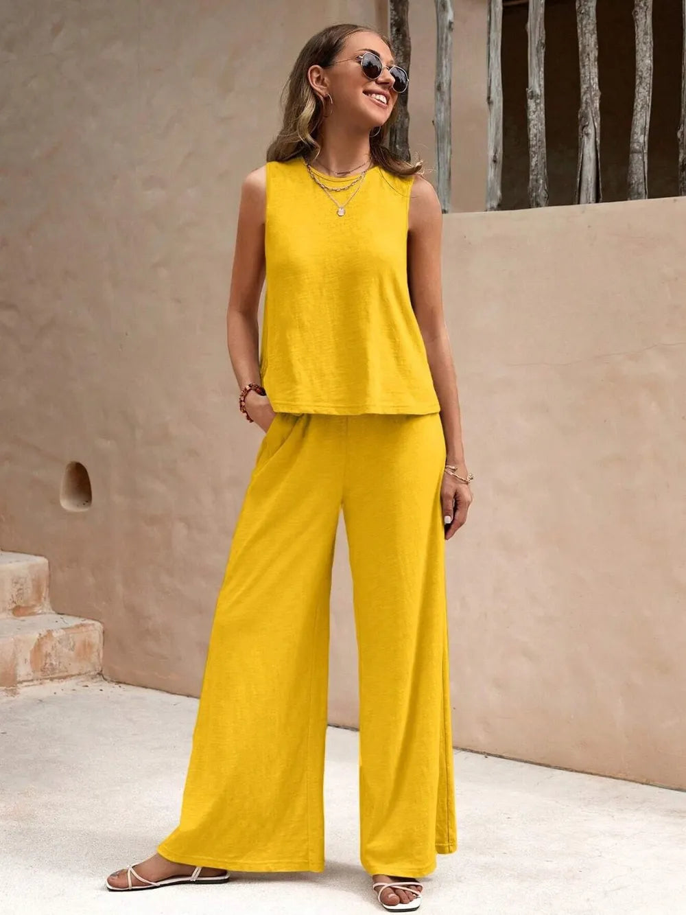 Model with hands in pockets posing in a gold yellow sleeveless round neck top and wide leg pants set with sunglasses