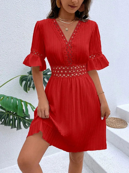 Woman wearing a vibrant red V-neck mini dress with textured vertical striping, featuring crochet lace trim along the neckline, waist cutouts, and flounce sleeve cuffs, styled with layered gold necklaces.