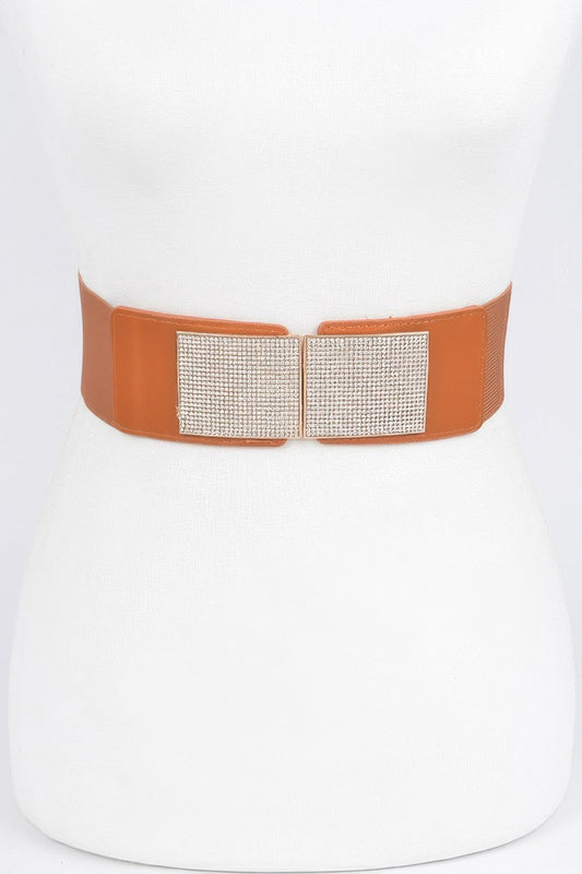 Front view of a camel brown elastic stretch belt with a large rectangular rhinestone-encrusted buckle, styled around a white dress mannequin against a light background.