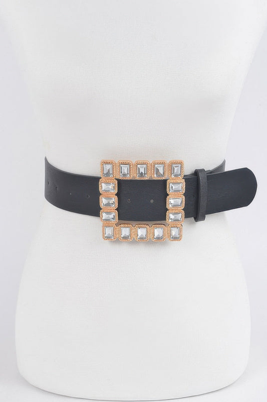 Front view of a black belt featuring a large square gold-tone buckle studded with clear crystal gemstones, styled on a white dress mannequin against a light background.