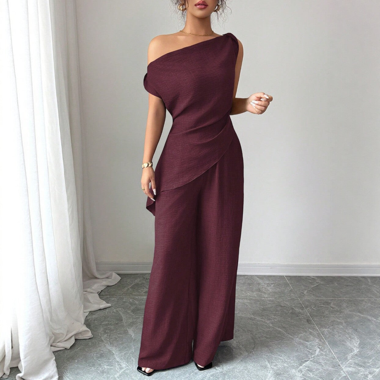 Woman wearing a wine red casual two piece set featuring an asymmetric one-shoulder top with a layered ruffle hem and matching high-waisted wide-leg pants.