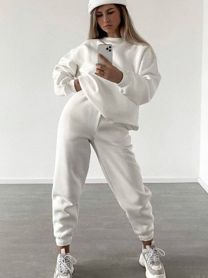 Woman wearing a white loose-fit crewneck sweatshirt and matching jogger pants two-piece set, taking a mirror selfie with a smartphone.