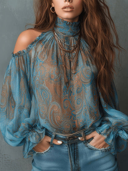 Woman wearing a peacock green retro cashew paisley print off-shoulder blouse with a high ruffled mock neck and dramatic lantern sleeves, styled with blue denim jeans.