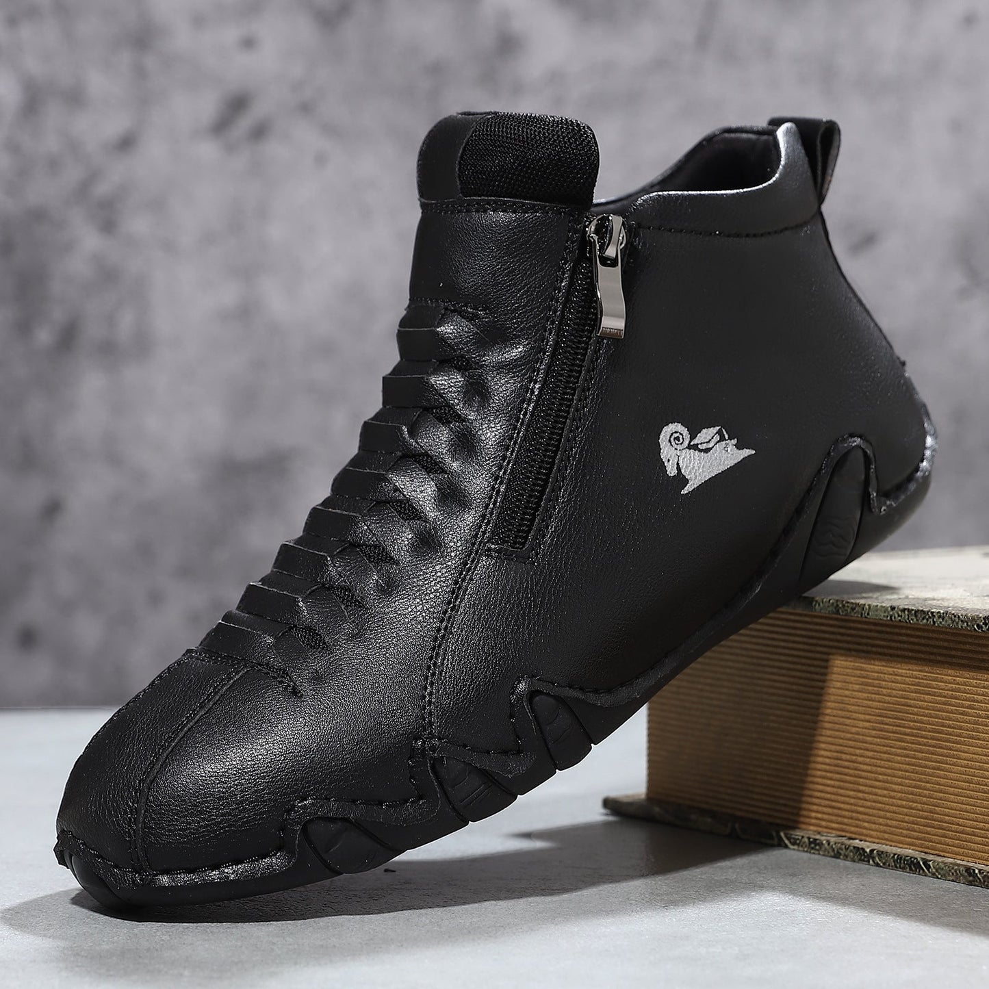 Black high-top athletic sneakers with a textured finish and side zipper, photographed on a wooden box.