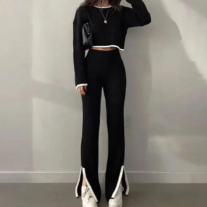 Woman wearing a black ribbed knit two-piece set featuring a long-sleeve crop top and matching slim pants with white trim detail, holding a black handbag.