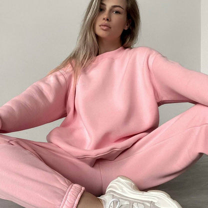 Woman wearing a pink loose-fit crewneck sweatshirt and matching jogger pants two-piece set, styled with white sneakers.