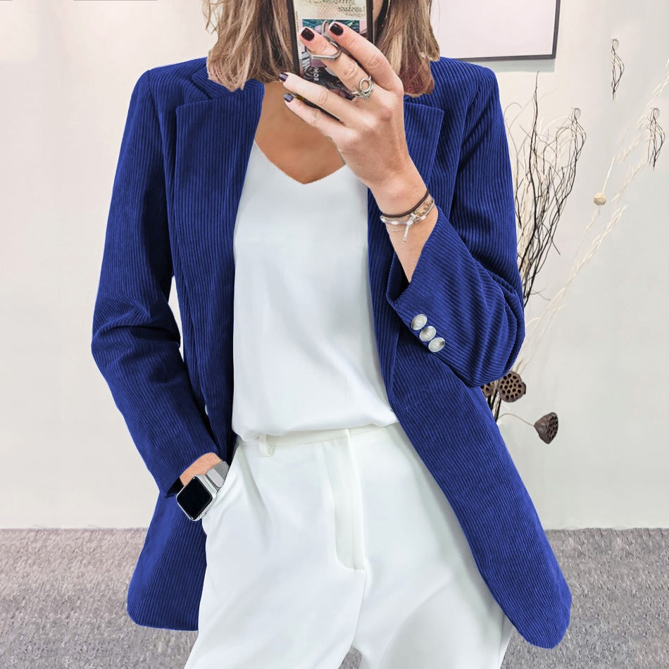 A woman wearing a blue slim-fit corduroy blazer over a white top and white trousers, taking a mirror selfie indoors.