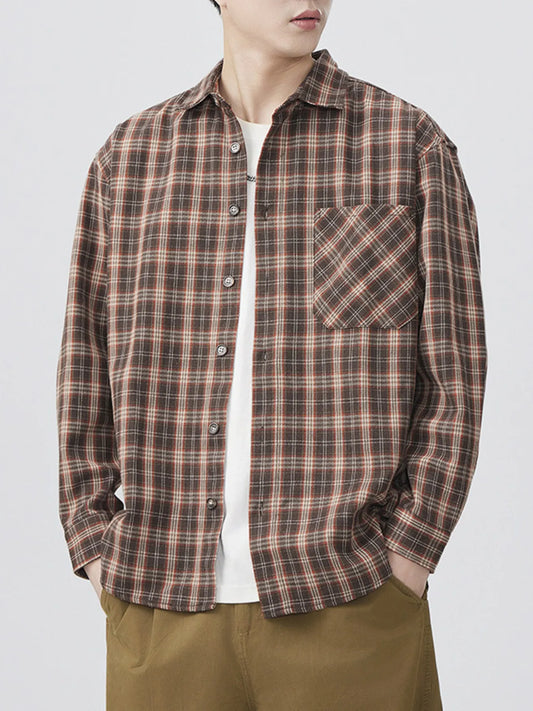 A man wearing a casual brown and black plaid long-sleeve button-up shirt over a white t-shirt.