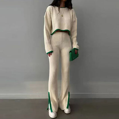 Woman wearing a white knit two-piece set featuring a long-sleeve crop top and matching slim slit pants with green trim details, standing indoors.