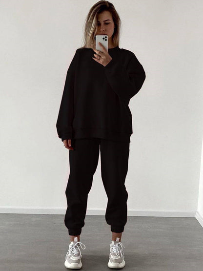 Woman wearing a black loose-fit crewneck sweatshirt and matching jogger pants two-piece set, styled with white sneakers.