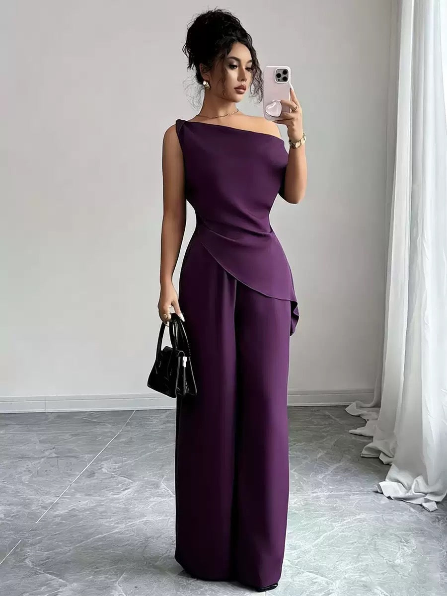 Woman taking a mirror selfie wearing a mauve pink casual two-piece set featuring a draped off-the-shoulder top with a diagonal front fold and matching high-waisted wide-leg pants, holding a black handbag and smartphone.
