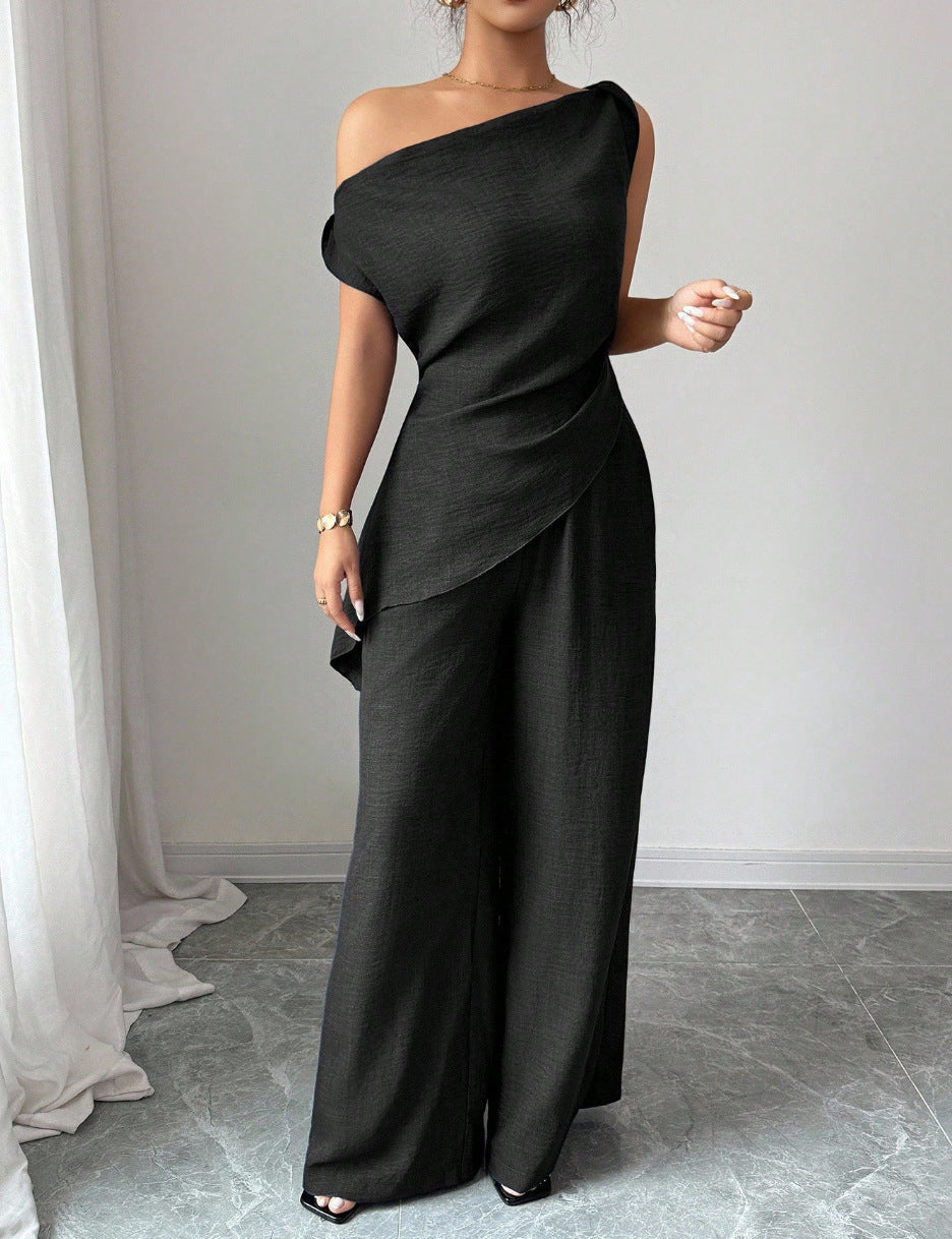 Woman wearing a black casual two piece set featuring an asymmetric one-shoulder top with a layered drape and matching high-waisted wide-leg pants.