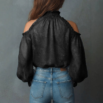 Back view of a woman wearing a black retro cashew print off-shoulder blouse with a high ruffled collar and dramatic lantern sleeves, styled with blue denim jeans.